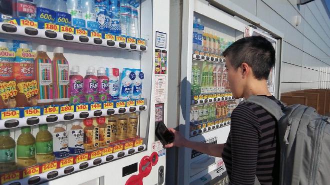 I hold up my phone to a drink vending machine to contactlessly pay for a bottle of milk tea.