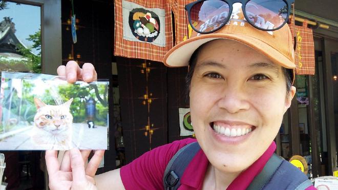 I hold a postcard with a closeup of the ginger shrine cat.